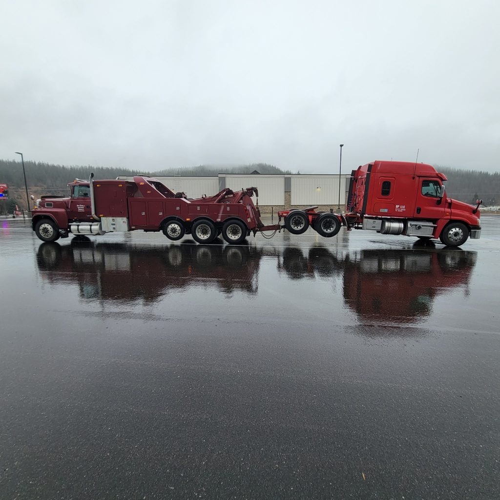 Heavy-duty tow truck hauling a commercial semi-truck trailer on the highway at sunset